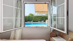 Et soveværelse med udsigt til en swimmingpool, en fletstol og en seng.