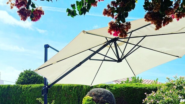 En terrasse med fletmøbler, en pool og en stor parasol.