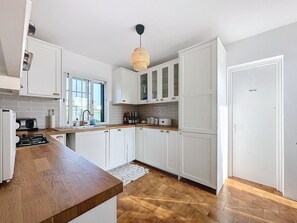 A modern kitchen with white cabinets, a wooden countertop, and a hanging light fixture.