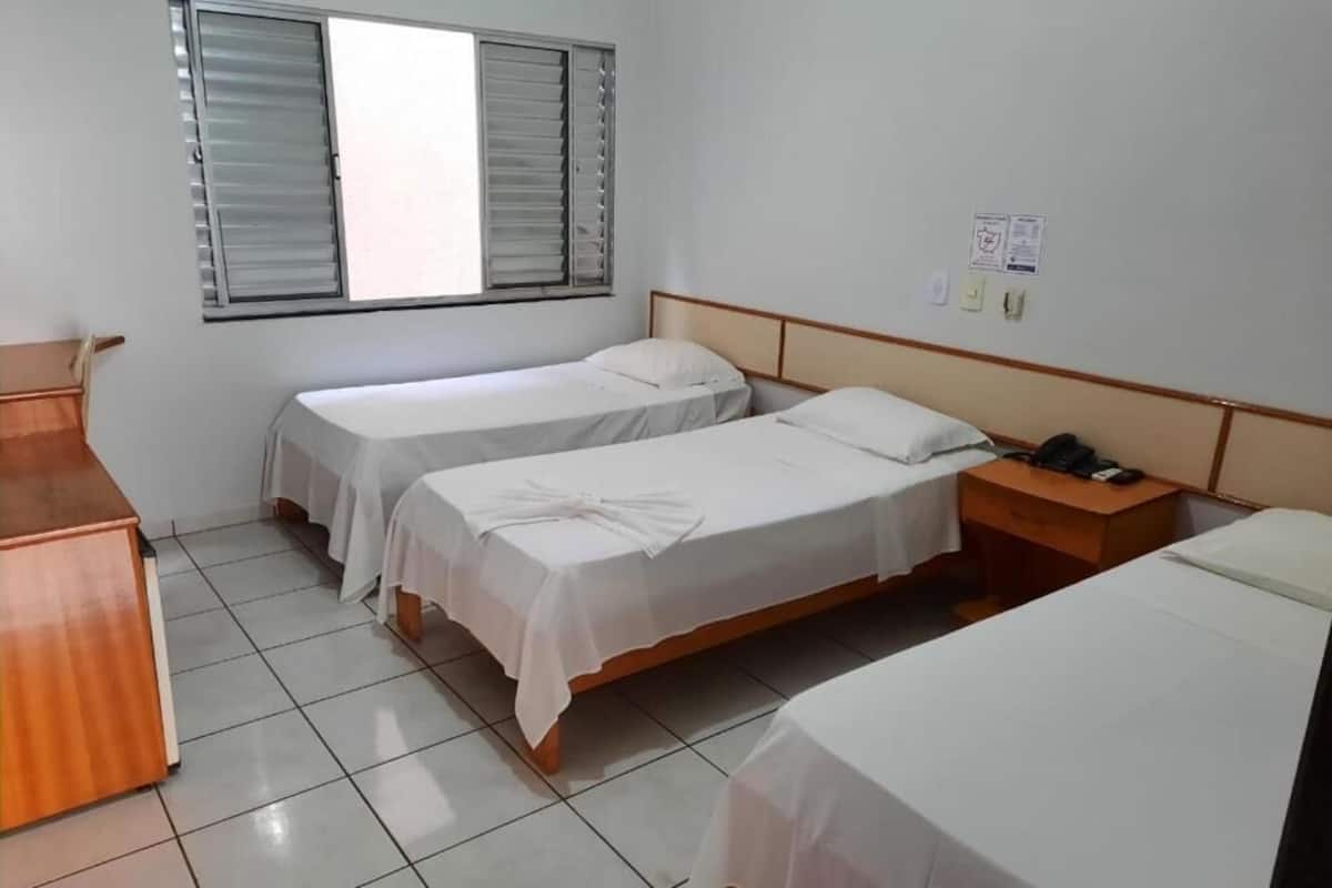 Una habitación con dos camas individuales, un escritorio de madera y una ventana con persianas.