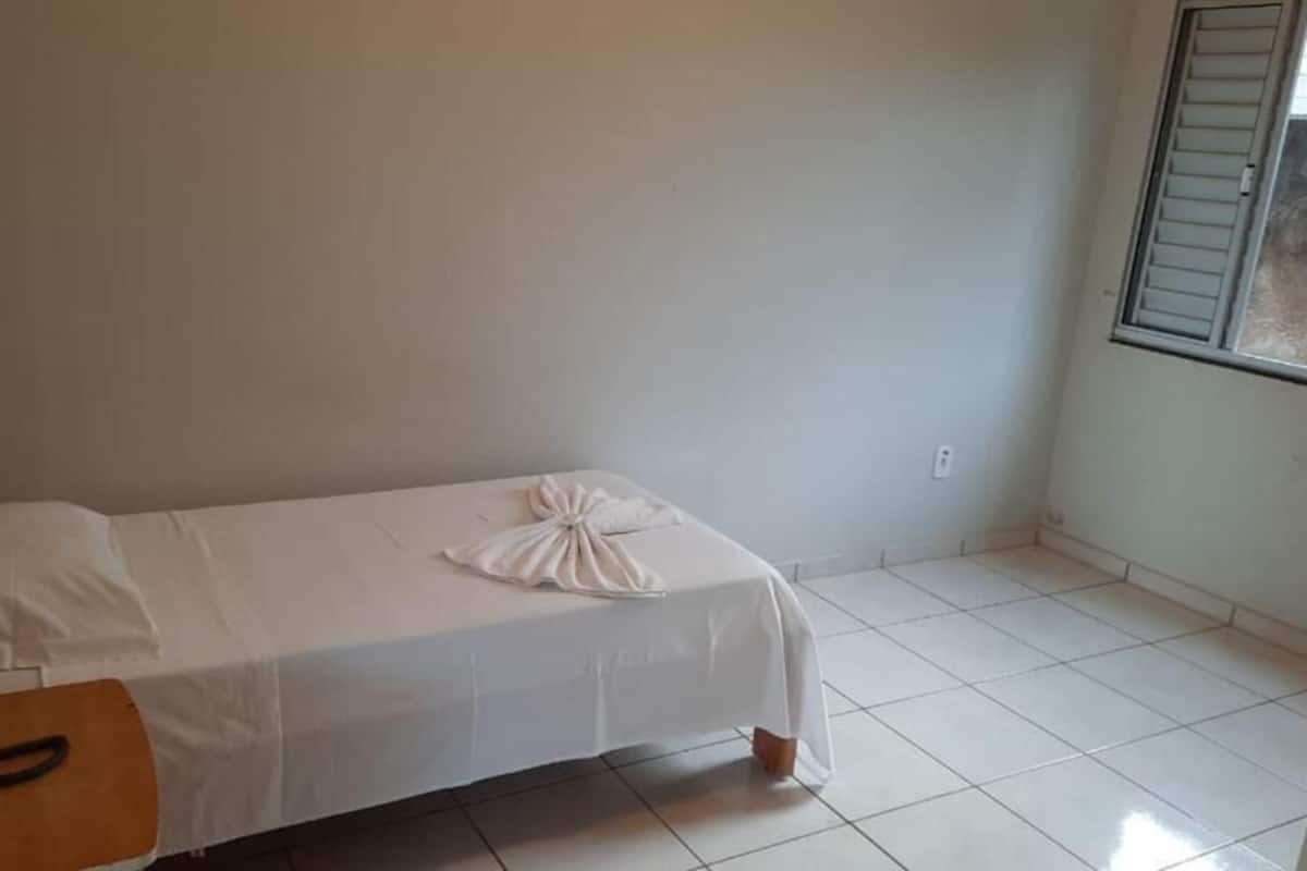 Una habitación pequeña y ordenada con una cama individual, una mesita de noche de madera y una ventana con persianas.