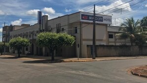 Ein Hotel namens "BRAO CITY HOTEL" mit einem Schild, an einer von Bäumen gesäumten Straße unter blauem Himmel.