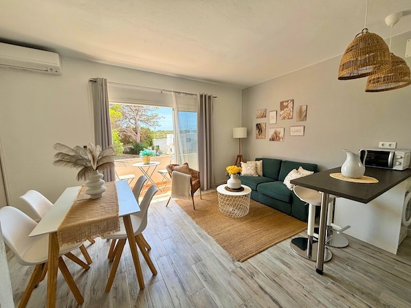 A modern living room with a dining area, a sofa, a coffee table, and a view of the outdoors. - Apartment 'Ca Nostra' with Balcony and Wi-Fi (Cala en Porter Menorca)