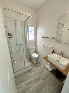 Un baño moderno con cabina de ducha de vidrio, inodoro, lavabo con espejo y tocador de madera.