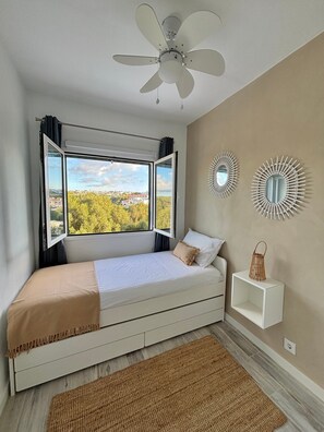 Un dormitorio con cama, ventilador de techo, ventana con cortinas y espejos decorativos en la pared.