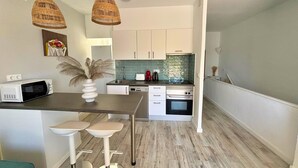 Une cuisine compacte comprenant un coin repas, des meubles blancs, un four à micro-ondes, un grille-pain et un évier.