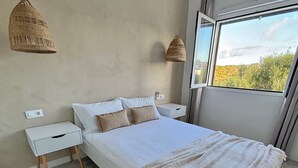 Une chambre à coucher avec un lit, des tables de chevet, un tapis tissé et une fenêtre donnant sur un beau paysage.
