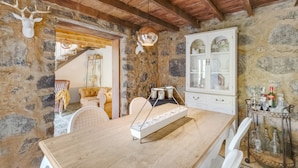 A rustic stone wall, wooden ceiling beams, a dining table with white chairs, a cabinet with glassware, and a deer skull decoration. - Holiday Home 'Caldera De Taburiente Rural' with Mountain View, Private Terrace and Wi-Fi (El Paso)