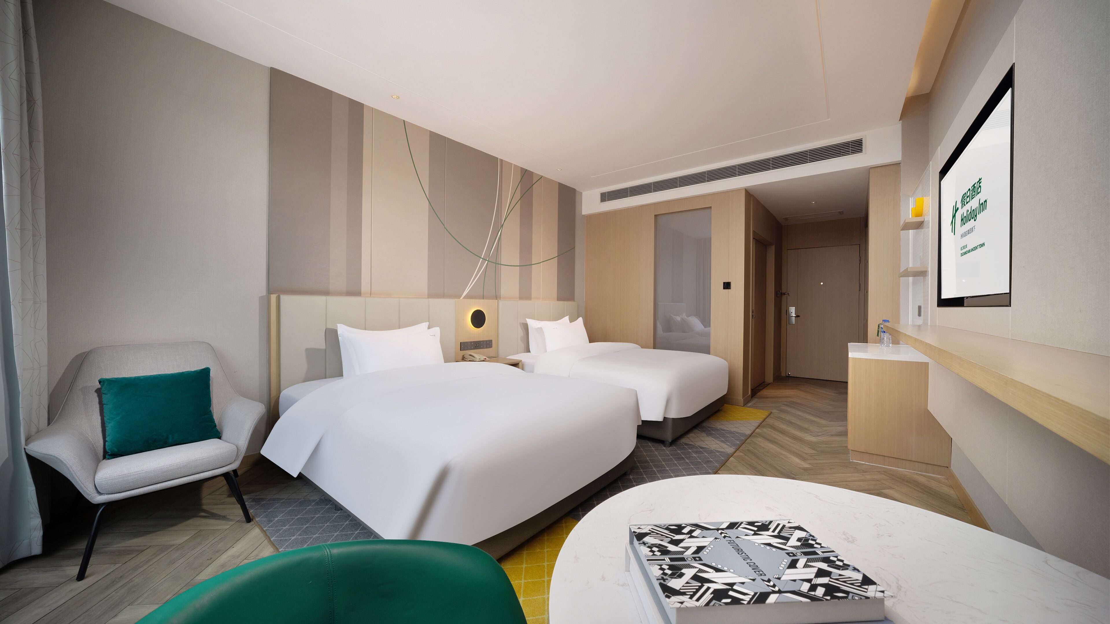 Quarto de hotel com duas camas, uma escrivaninha, uma cadeira e uma mesinha.