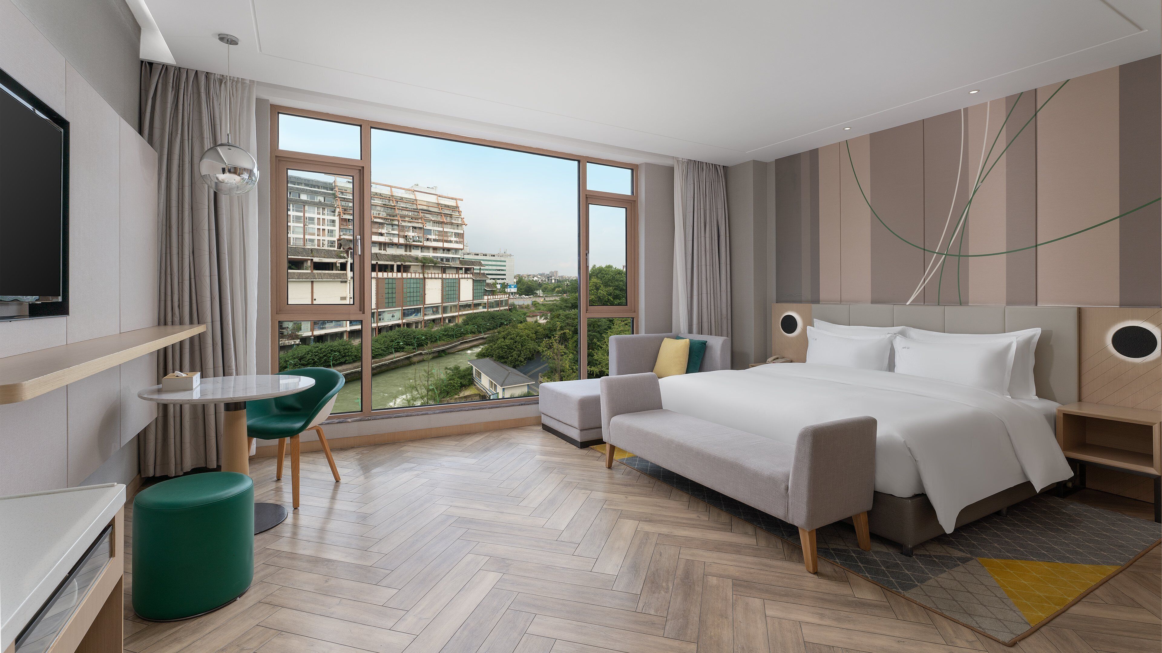 A modern hotel room with a large window, a bed, a desk, and a green chair.