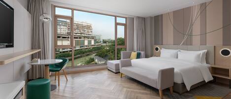 A modern hotel room with a large window, a bed, a desk, and a green chair.