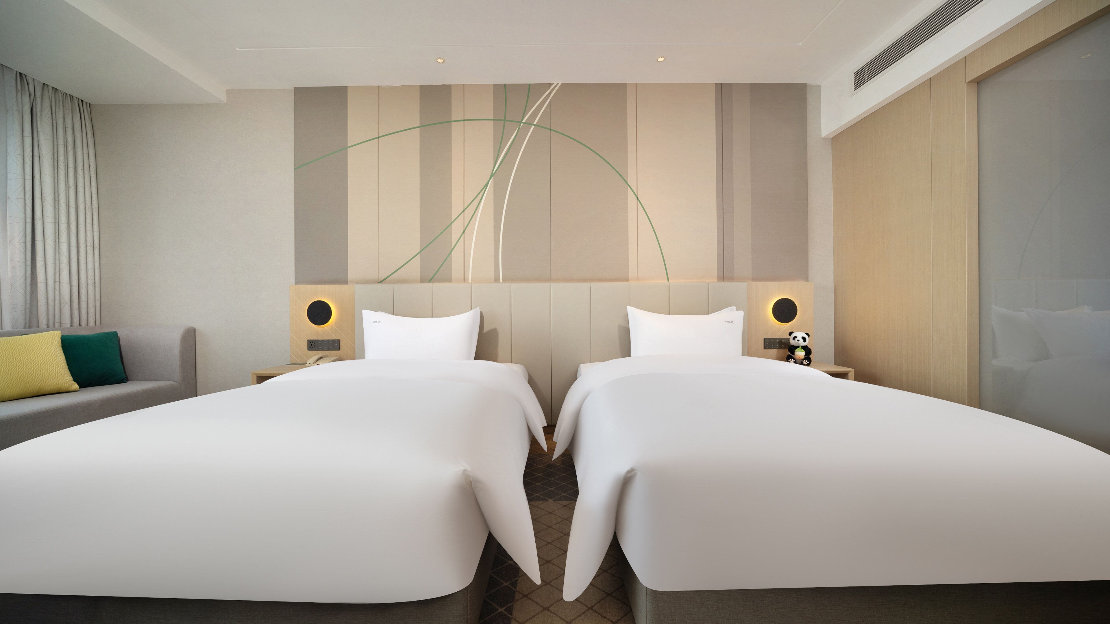 Une chambre d’hôtel avec deux lits, un canapé et une lampe fixée au mur.