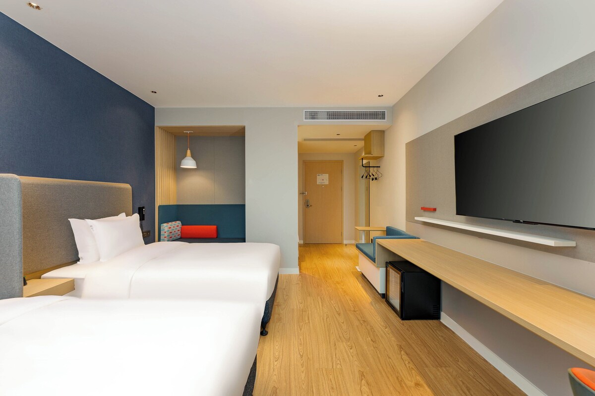 Una camera d'albergo con un letto grande, una TV fissata al muro e una scrivania con una sedia.