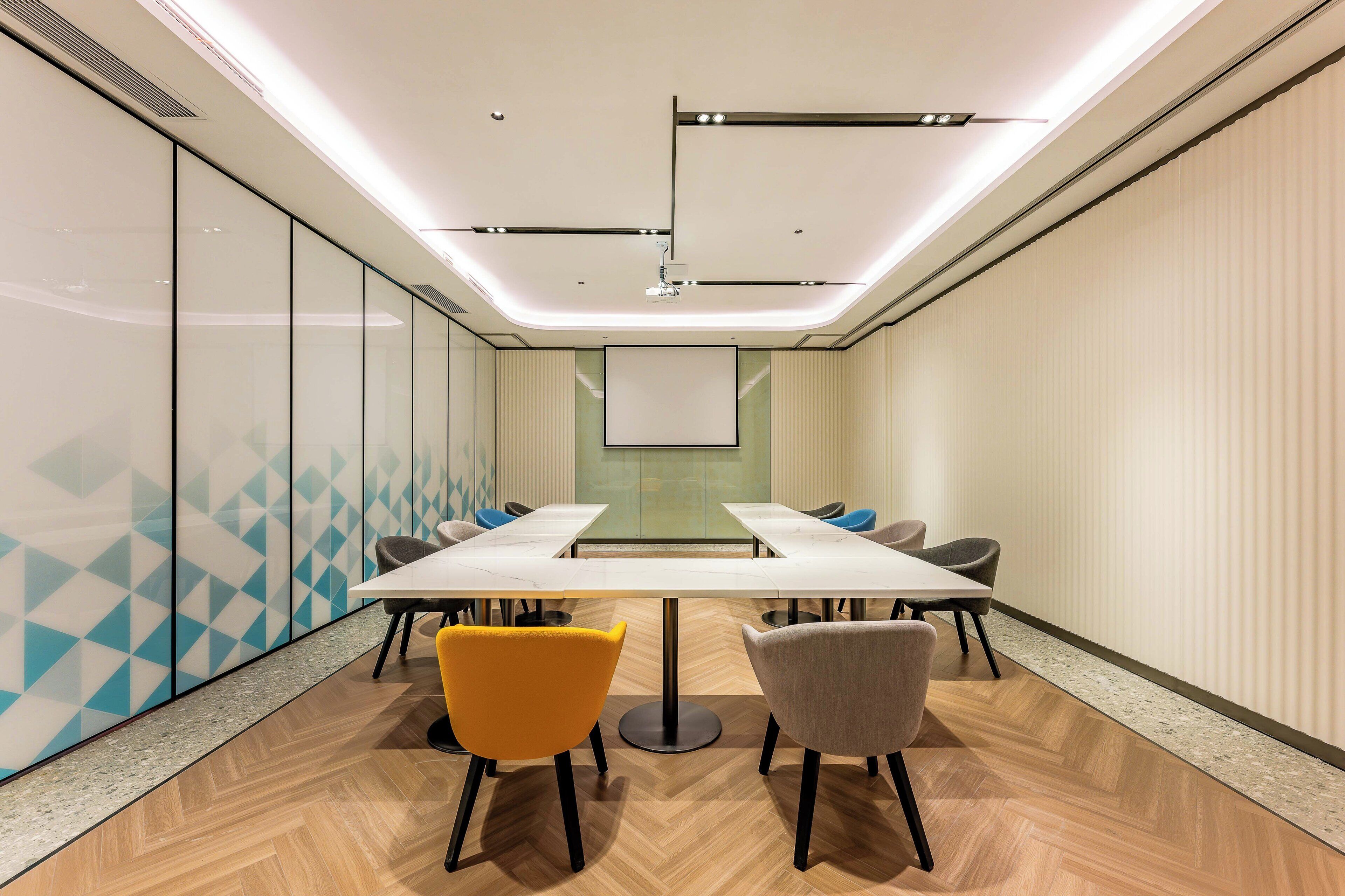 A conference room with a long table, four chairs, and a projector screen.