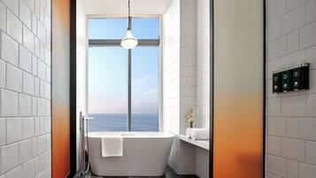 Un baño moderno con una bañera independiente, un ventanal grande y vista al mar.