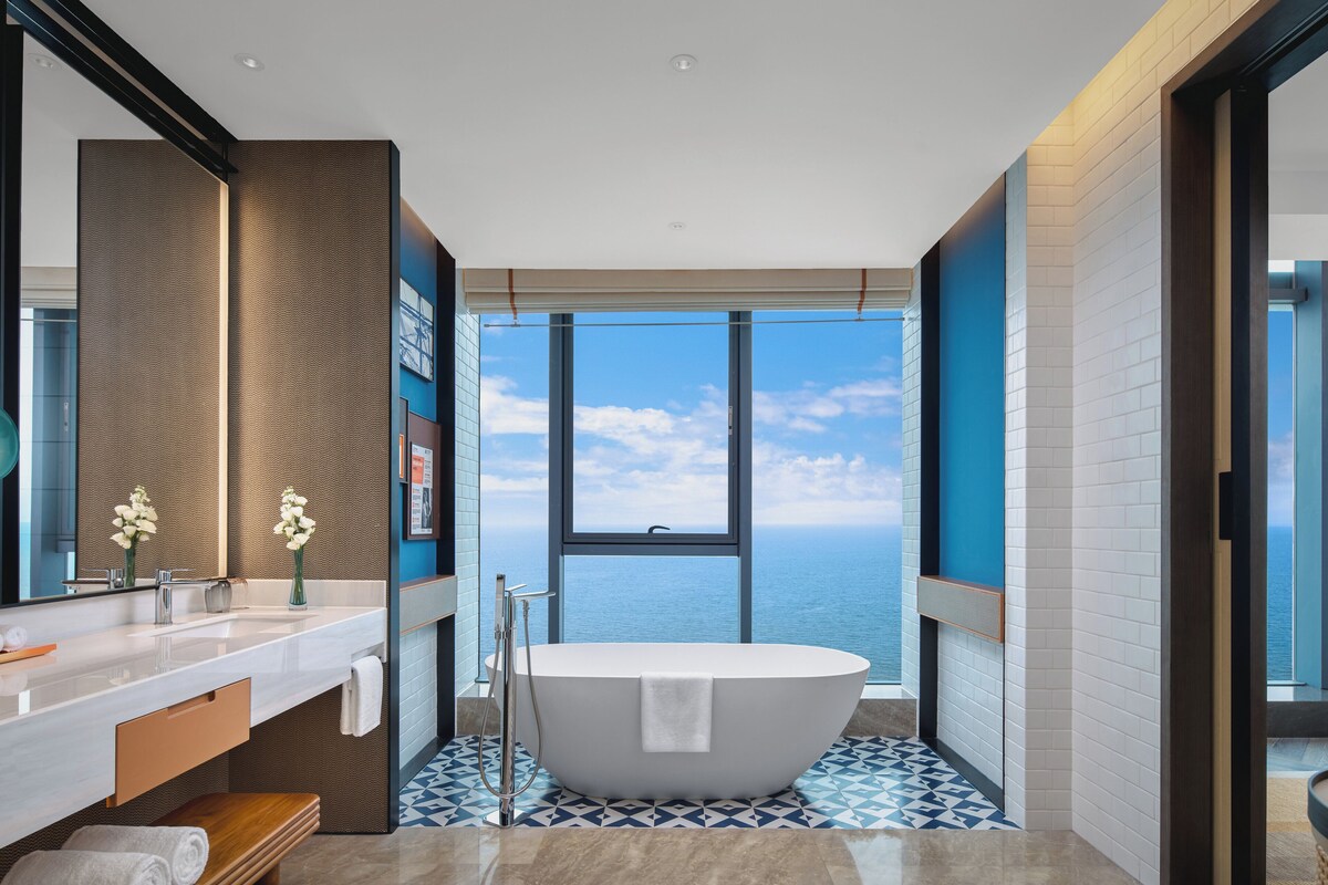 Une salle de bain moderne avec une baignoire sur pieds, un grand miroir et une vue sur la mer.