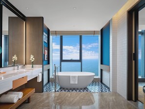 Un baño moderno con una bañera independiente, un espejo grande y vistas al mar.