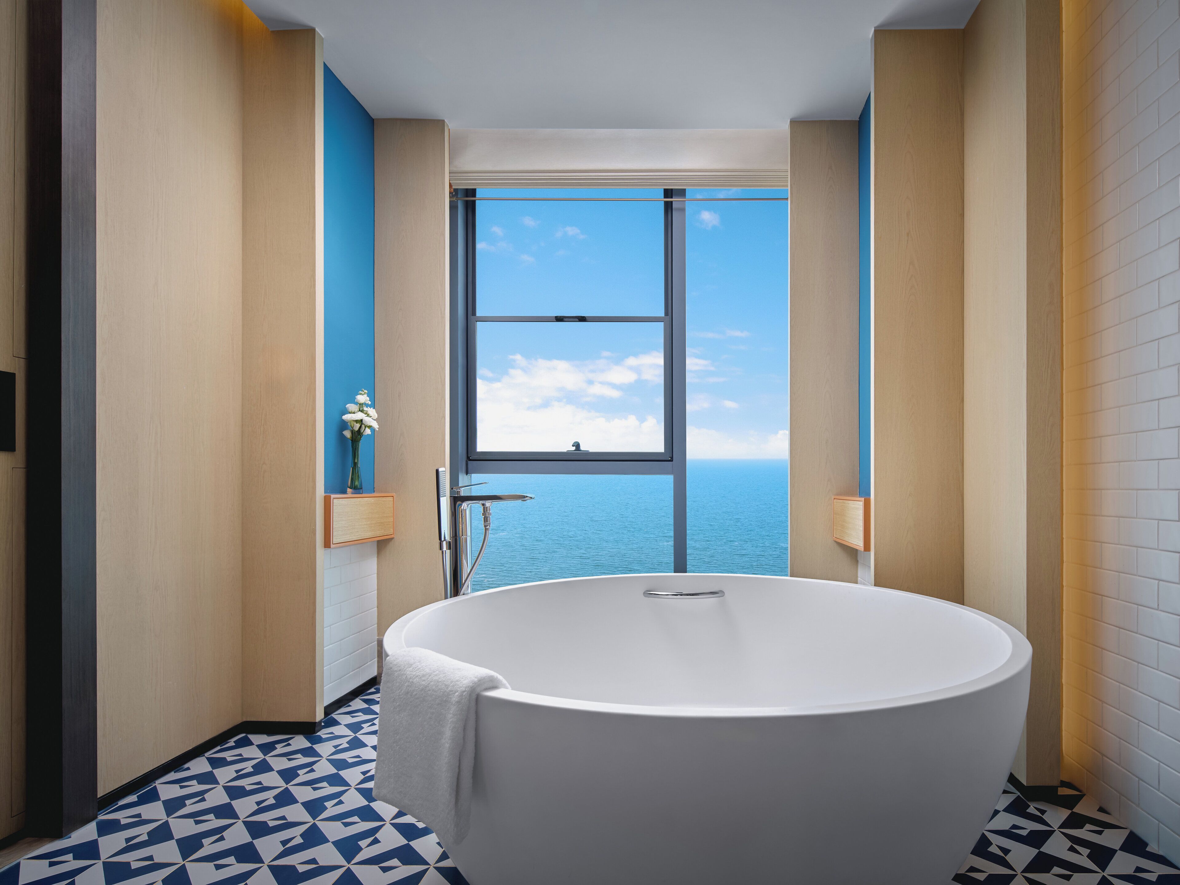 Un baño moderno con una bañera grande, un ventanal con vistas al mar y un suelo de diseño geométrico.