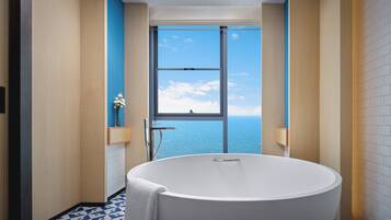 Un baño moderno con una bañera grande, un ventanal con vistas al mar y un suelo de diseño geométrico.