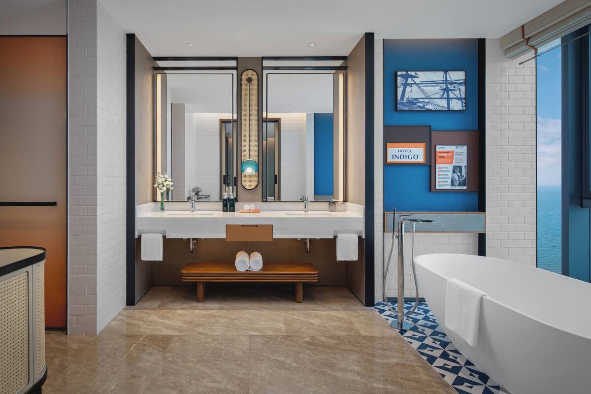 Een moderne badkamer met een grote spiegel, twee wasbakken, een bankje en een bad.