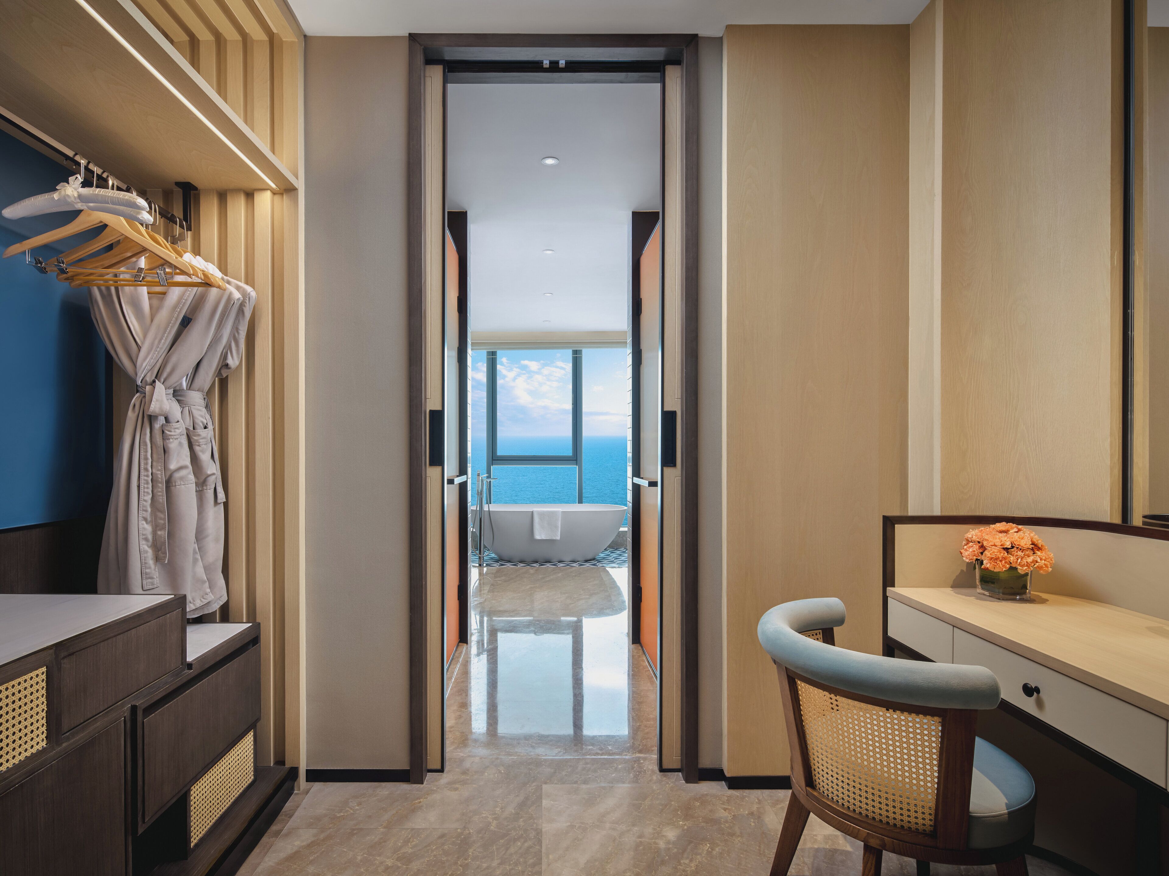 A modern hotel room with a view of the sea, a bathtub, and a desk with a chair.
