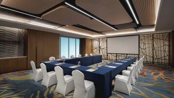 A conference room with a long table, white chairs, and a projector screen.