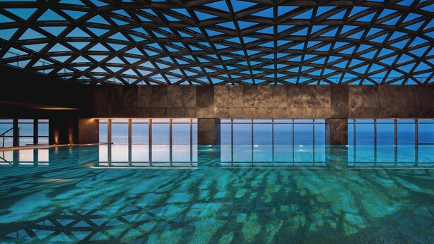 Una piscina interior con una estructura de techo geométrica y ventanas amplias.