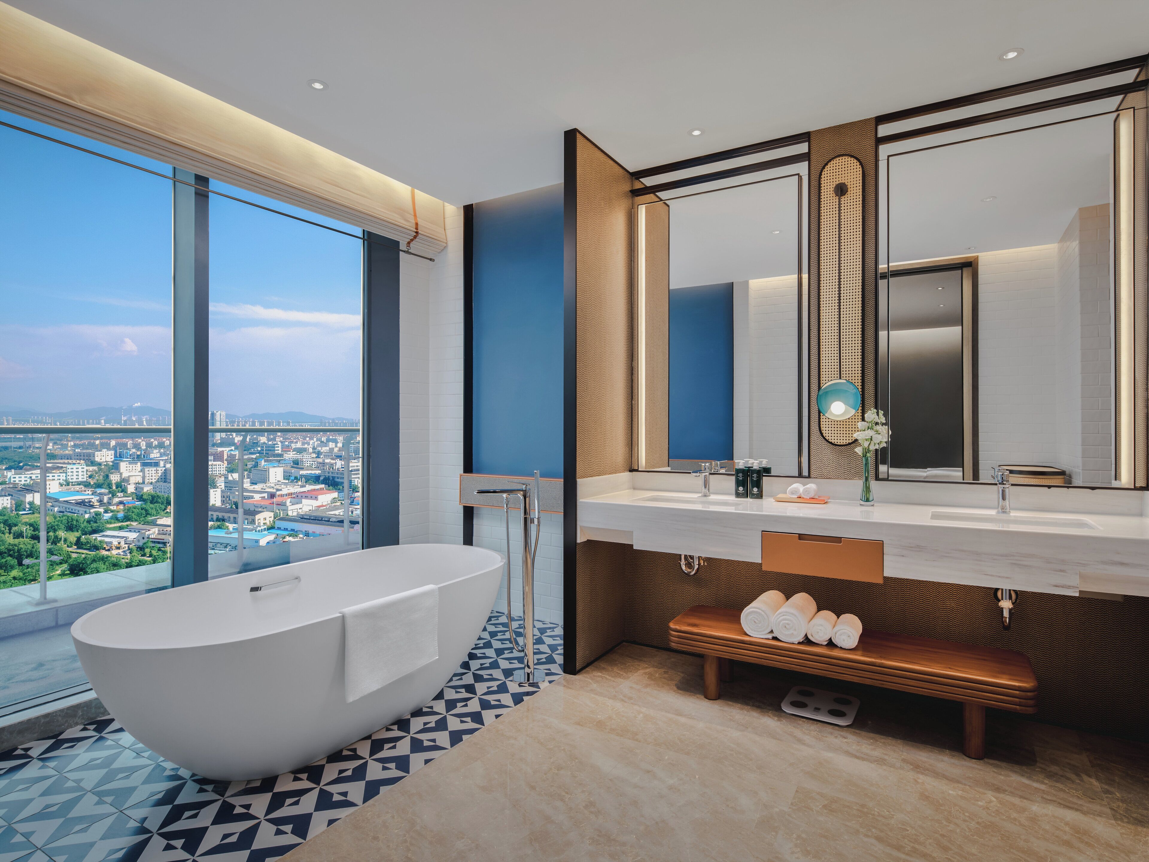 A modern bathroom with a large bathtub, a vanity with a mirror, and a bench with towels.