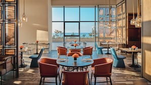 Un comedor moderno con mesas redondas, sillas anaranjadas y ventanas amplias con vistas al mar.