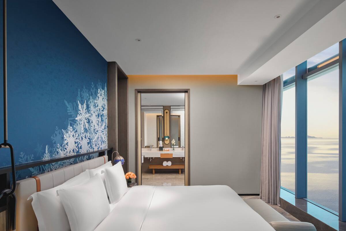 Een moderne hotelkamer met een groot bed, een badkamer met spiegel en uitzicht op zee.