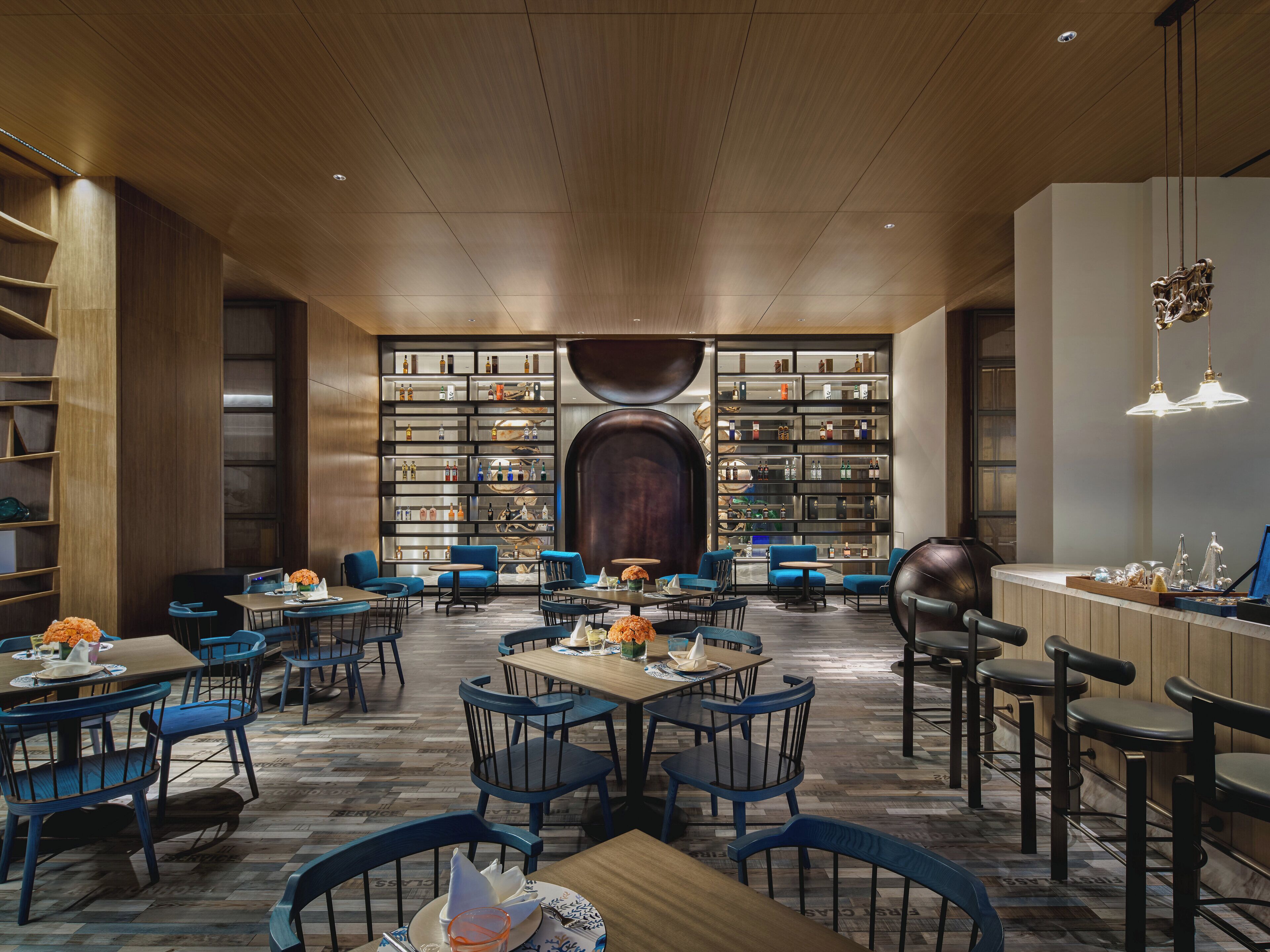 A spacious, modern interior with a central seating area, a bar, and a large bookshelf filled with various items.