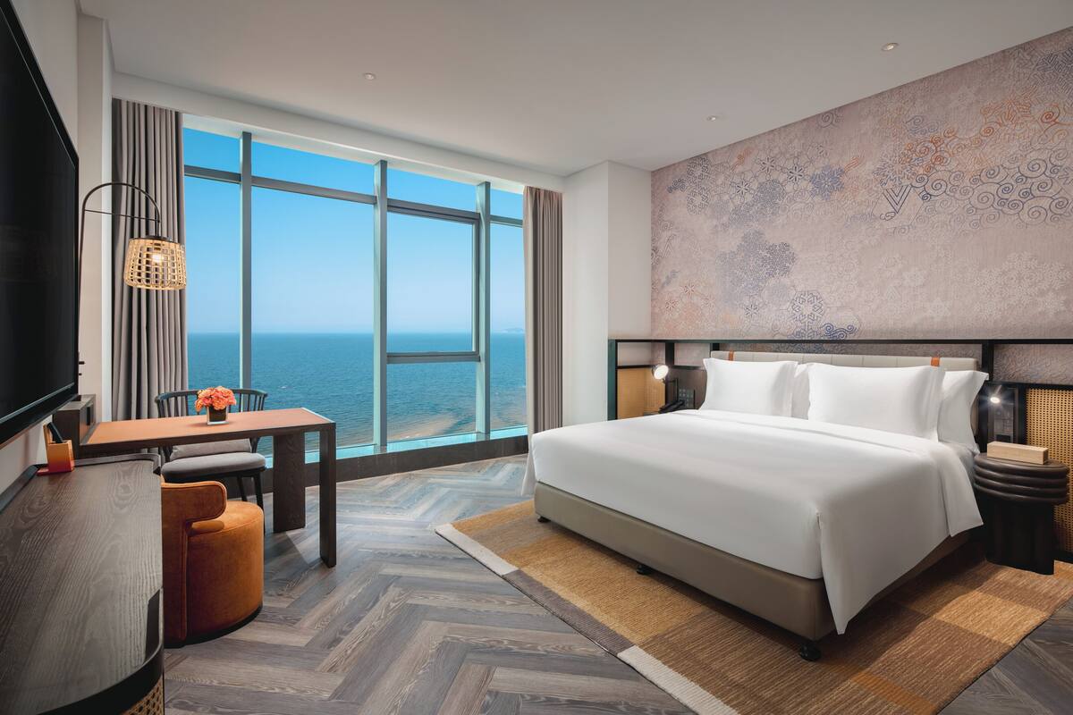 Een hotelkamer met een groot raam, een bed, een bureau en een stoel.