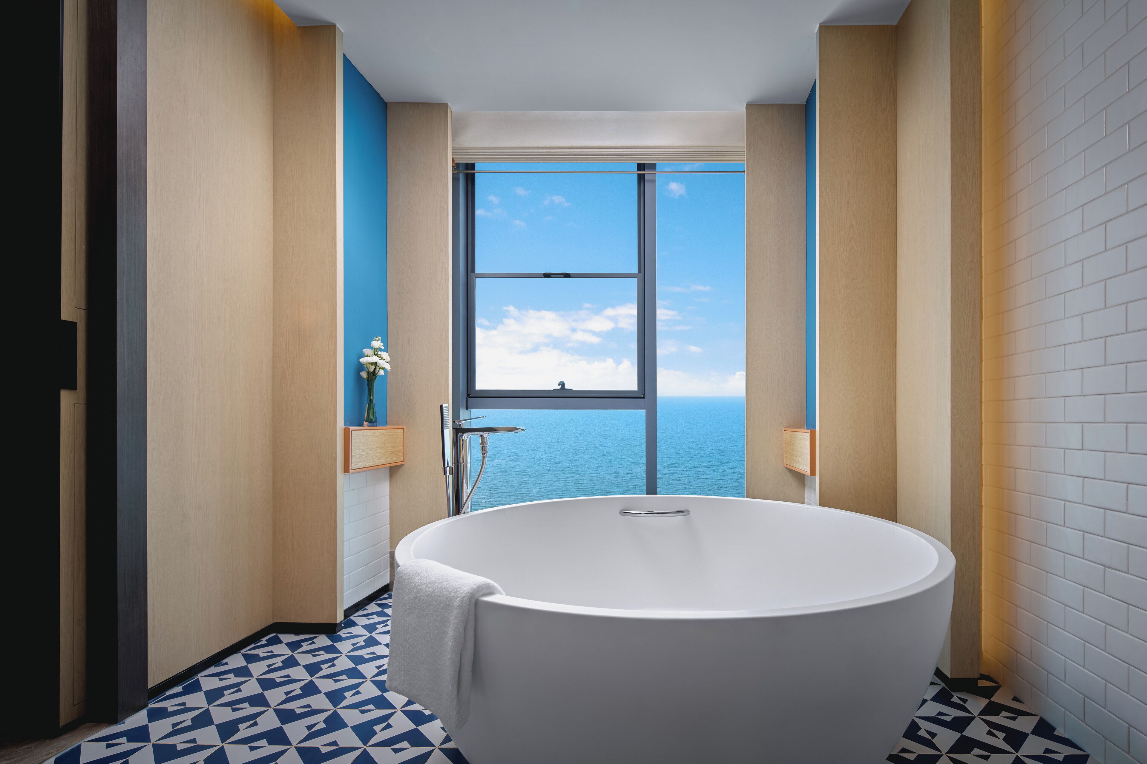 Un baño moderno con una bañera independiente, un amplio ventanal con vistas al mar y un suelo con estampado geométrico.
