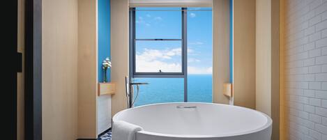 Un baño moderno con una bañera independiente, un amplio ventanal con vistas al mar y un suelo con estampado geométrico.
