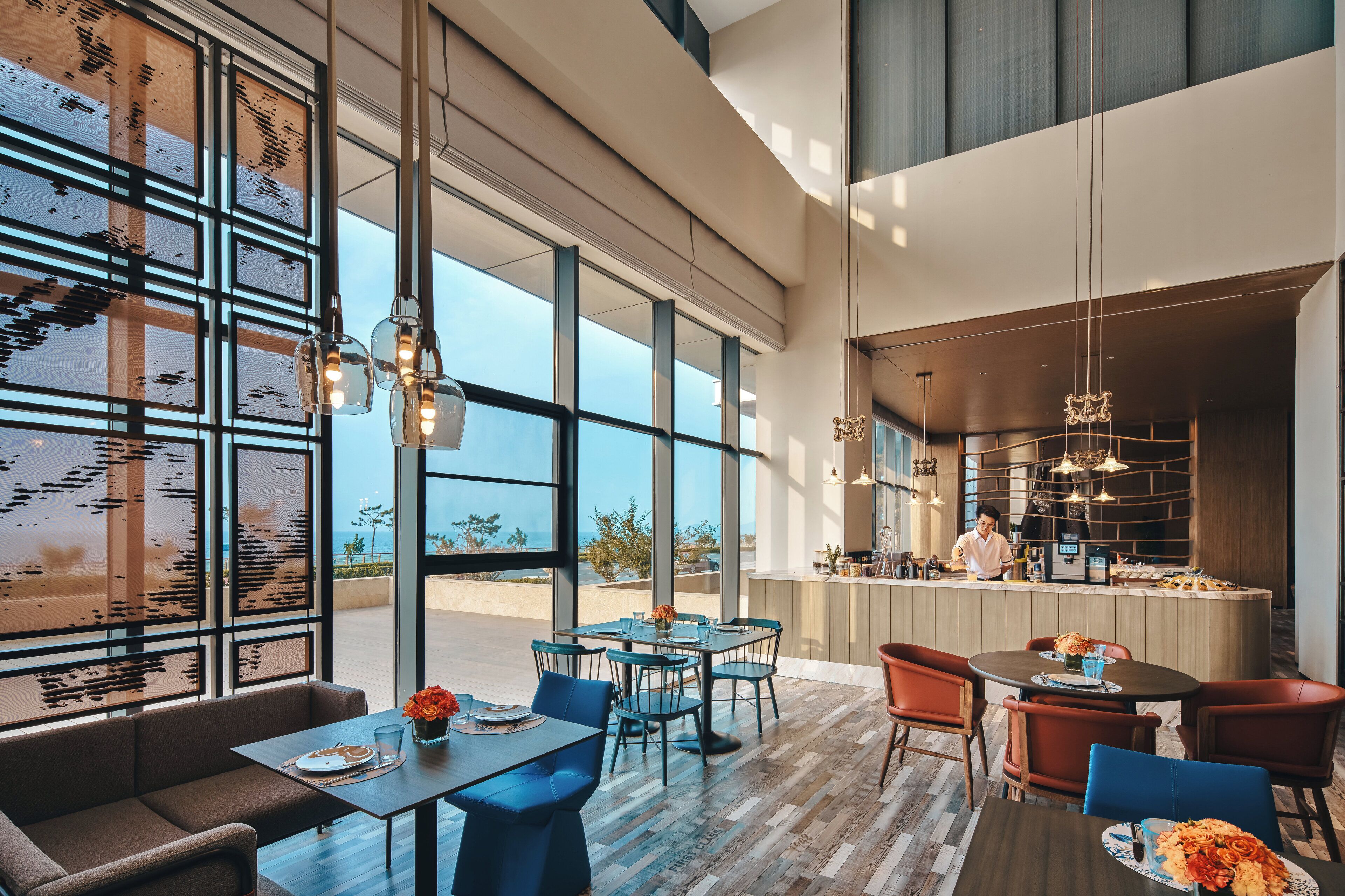 A modern restaurant with large windows, a bar area, and seating arrangements.