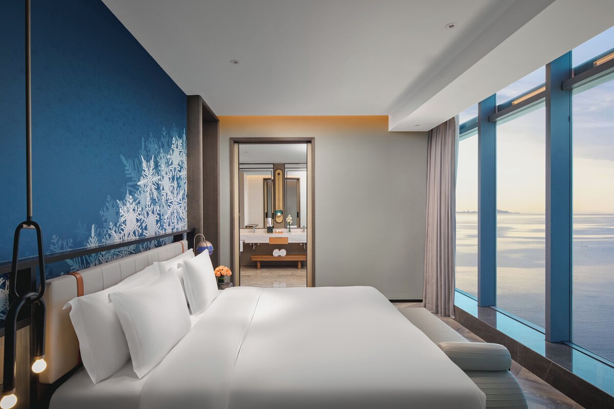 Une chambre d’hôtel moderne avec un grand lit, une salle de bain avec un miroir et une vue sur la mer.