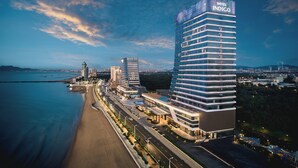 Un hotel moderno con un llamativo letrero que dice 'HOTEL INDIGO', ubicado junto a una costa con playa y una carretera que lleva al hotel.