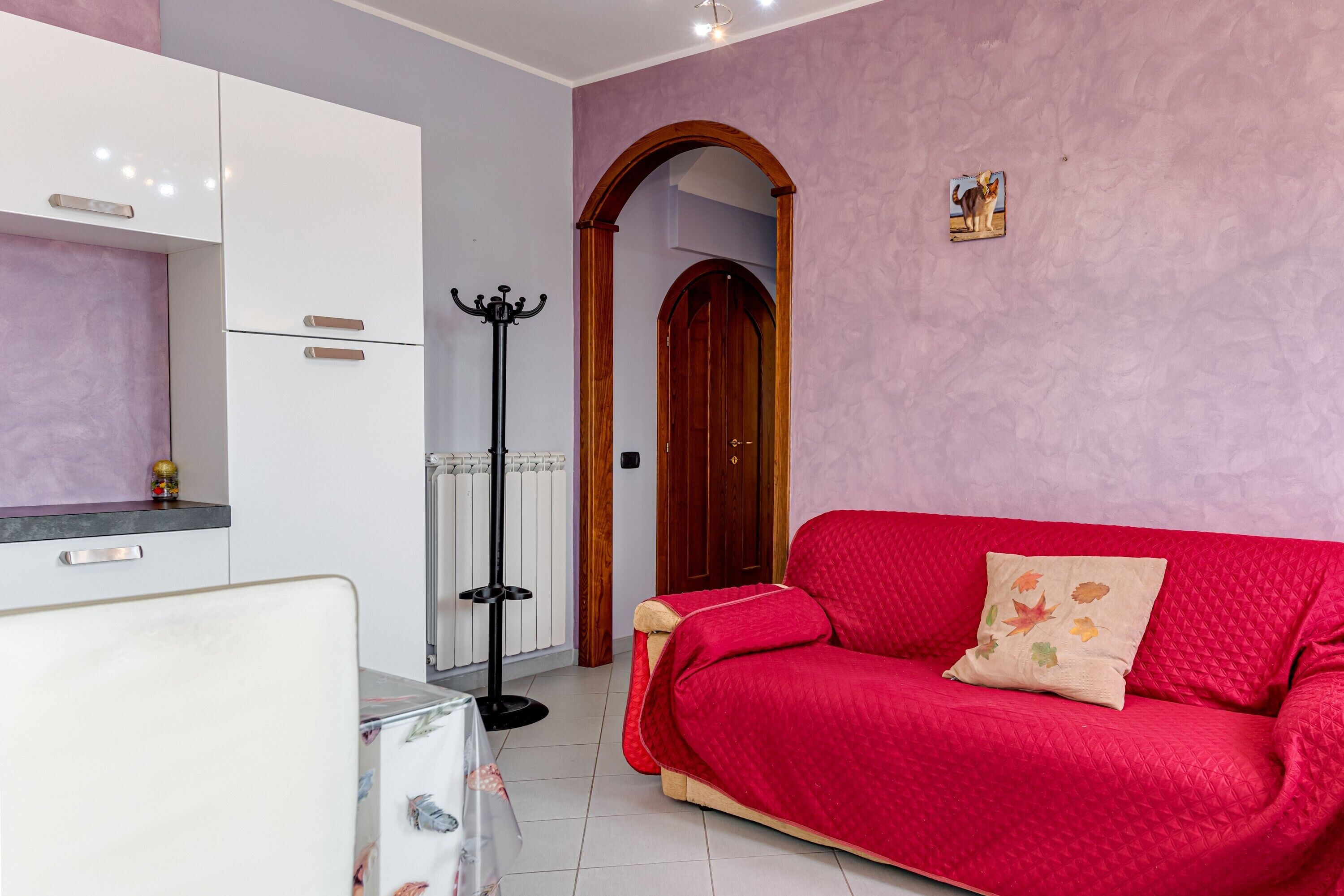 Ein Zimmer mit einer roten Couch, weißen Schränken, einem Kleiderständer und einer Holztür.