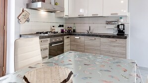 Une cuisine moderne avec des meubles blancs, une cuisinière à gaz, un évier et une table à manger recouverte d’une nappe à motifs de poissons.