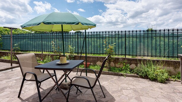 Une terrasse avec une table et des chaises, un parasol et une vue sur une clôture verte et des plantes.