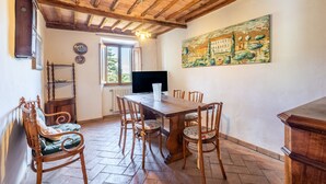 A dining area with a wooden table and chairs, a television, and a painting on the wall. - Apartment 'Villa Caselunghe' with Shared Pool, Wi-Fi and Air Conditioning (Siena)