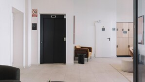 A modern hotel lobby with a black door, a seating area with a brown chair, and a wooden cabinet in the background. - Aspasios Sofia Apartments (Madrid)