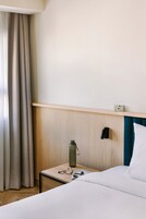 Ein Hotelzimmer mit einem Bett, einem Nachttisch mit einer Wasserflasche, Gläsern und einer Uhr.