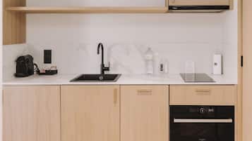 Une cuisine moderne dotée d’un évier noir, d’un lave-vaisselle encastré, de meubles en bois et d’un plan de travail sur lequel se trouvent une bouilloire, une bouteille et un petit appareil électroménager.