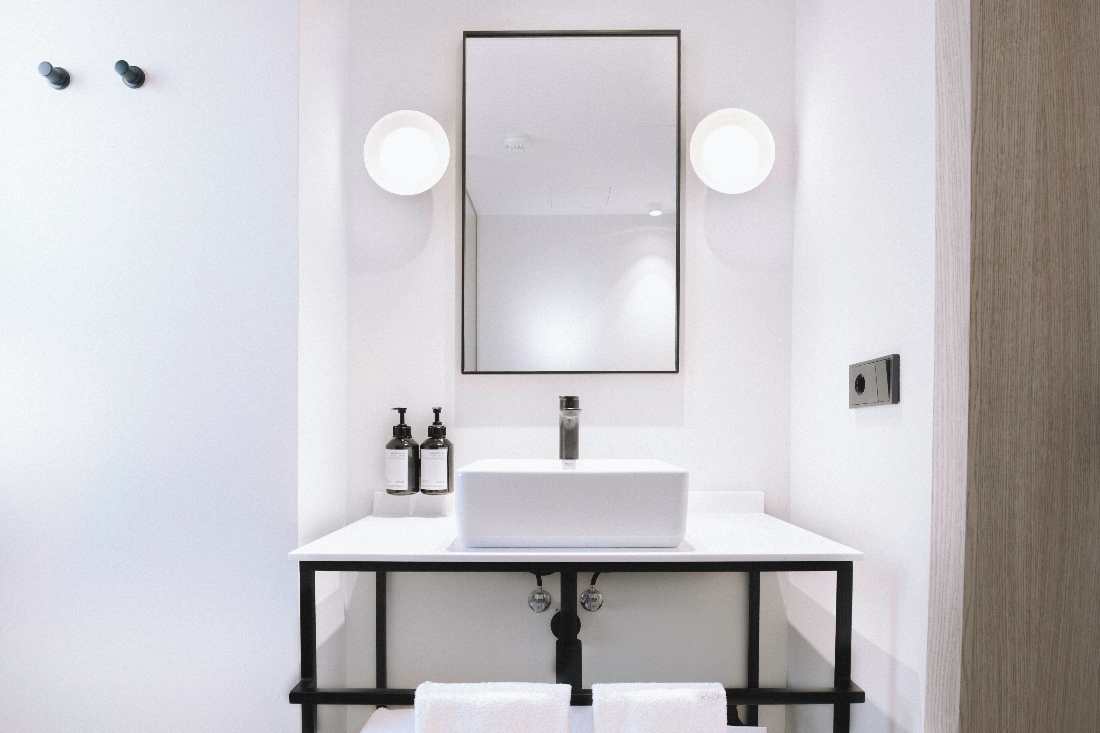 Un baño moderno con un lavamanos blanco, marco negro, dos luces redondas y un espejo.