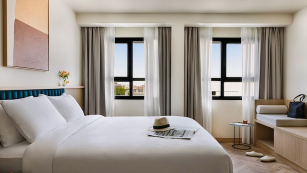 A hotel room with a large bed, a small table, a sofa, and a view of the city through large windows. - Aspasios Sofia Apartments (Madrid)