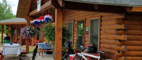 A rustic log cabin with a covered porch, outdoor seating, and a bicycle parked outside.