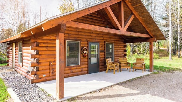 Eine Blockhütte mit Veranda, zwei Türen und einer kleinen Sitzgelegenheit im Freien.