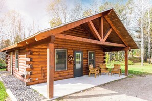 A log cabin with a porch, two doors, and a small outdoor seating area. - Perfect for Families & Friends, Pet Friendly, Horse Theme, Log Cabin, Fireplace (Mountain)