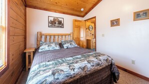 Ein Schlafzimmer mit Holzboden, einem Bett mit Bettwäsche mit Waldmotiv, einem kleinen Nachttisch und einer Tür zu einem Badezimmer.
